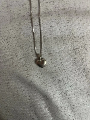 Silverhalsband med hjärthänge - Snyggt halsband i silverfärg med ett litet hjärthänge. Kedjan är tunn och enkel, vilket gör att hjärtat verkligen står i fokus. Perfekt accessoar för att ge din outfit en söt och stilren touch. Passar dig som gillar minimalistiska smycken.