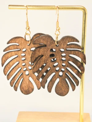 Ultralätta Bruna Monstera örhängen i trä - Unika örhängen i form av Monstera-blad, tillverkade i mörkbrunt trä med guldfärgade krokar. De har en snygg, naturlig look och är laserskurna för detaljerad form. Perfekta för dig som gillar växtinspirerade accessoarer och vill sticka ut.