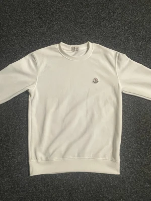 Vit sweatshirt från Moncler - Snygg vit sweatshirt från Moncler med klassisk rund halsringning och Moncler-logga broderad på bröstet. Tröjan har använts några gånger 