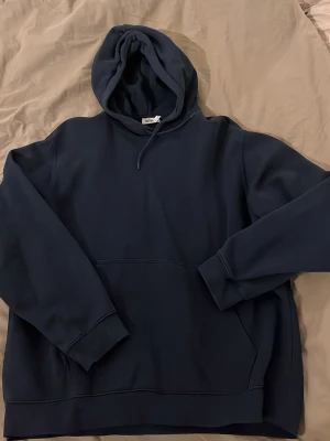 Mörkblå hoodie från Weekday - Snygg mörkblå hoodie från Weekday med klassisk huva och dragsko. Hoodien har en stor magficka och ribbade muddar vid ärmar och nederkant. Tillverkad i mjukt material som känns skönt mot huden. Perfekt för en avslappnad och stilren look.