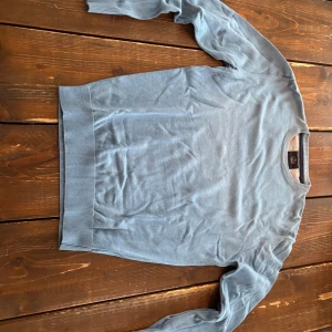 Ljusblå rundhalsad tröja - Snygg ljusblå tröja med rund halsringning och ribbade muddar vid ärmslut och nederkant. Tröjan har en clean look och är tillverkad i ett tunt, mjukt material som passar perfekt till lager på lager.