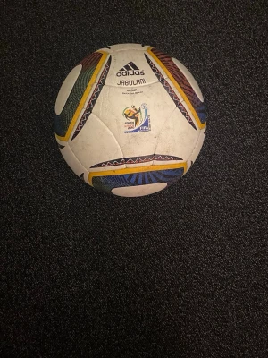 Adidas Jabulani FIFA World Cup boll - Säljer en Adidas Jabulani Glider fotboll, officiell matchbollsreplika från FIFA World Cup 2010 i Sydafrika. Bollen är vit med färgglada detaljer i gult, rött, grönt och blått samt mönster runt panelerna. Perfekt för träning och spel på alla nivåer.