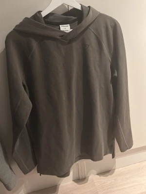 Gymshark Hoodie - Snygg olivgrön hoodie från Gymshark med diskret logga på bröstet. Hoodien har en klassisk huva och är tillverkad i ett mjukt och bekvämt material, perfekt för både träning och chill. Raglanärmar ger en sportig vibe och extra rörelsefrihet.