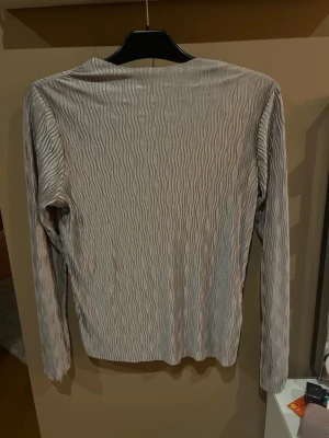Ljusgrå/lila ribbad långärmad topp nypris 700 - Säljer en ljusgrå/lila långärmad topp med vågigt ribbat mönster. Toppen har en slim passform och är tillverkad i ett mjukt syntetmaterial. Perfekt att styla med jeans eller kjol för en trendig look.