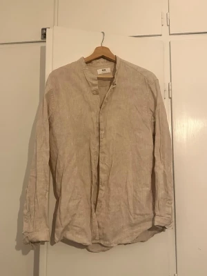 Beige linneskjorta från Uniqlo - Beige  skjorta från Uniqlo i linen. Skjortan har en enkel, avslappnad passform och står upp med en liten krage utan slag. Perfekt inför sommaren. Aldrig använd. Nyskick!