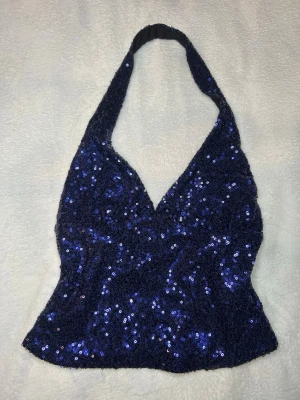 Marinblå paljett halterneck topp - Glittrig marinblå halterneck topp täckt med paljetter. Toppen har v-ringning och är ärmlös med en snygg croppad passform. Perfekt för att sticka ut och skapa en festlig look.