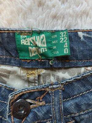 Blå bootcut low waist jeans - Snygga blå bootcut jeans från Bershka med slitna detaljer och ljusare partier framtill. Klassisk femficksmodell med låg midja och knappgylf. Perfekta för en avslappnad och trendig look.