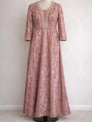 Glittrig rosa långklänning med paljetter - Elegant långklänning i rosa med glittriga paljetter. Klänningen har trekvartsärm och dekorativa detaljer längs halsen och ärmsluten. Perfekt för speciella tillfällen när du vill sticka ut.