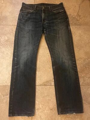 Levi's 514  33/34 - Säljer ett par Levi's 514 jeans i mörkblå tvätt med klassisk femficksdesign och raka ben. Jeansen har snygga slitningar och kontrastsömmar, samt den ikoniska läderlappen bak i midjan. Perfekta för dig som gillar en tidlös och avslappnad look. Skriv vid frågor eller funderingar!😊
