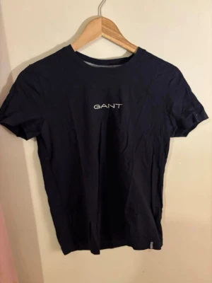 Mörkblå GANT t-shirt i bomull - Snygg mörkblå t-shirt från GANT med klassisk rund hals och vit broderad logga på bröstet. Tillverkad i mjuk bomull och har en normal passform. Använd fåtal gånger 