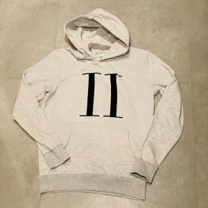 Les Deux jeans - Snygg ljusgrå hoodie från Les Deux med stor svart romersk siffra II på bröstet. Klassisk huva och ribbade muddar vid ärmar och nederkant. Tillverkad i mjukt bomullsmaterial som känns skönt mot huden. Perfekt för en avslappnad och trendig look.