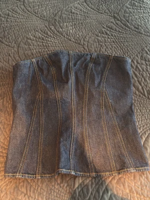 Mörkblå denimkorsett med dragkedja - Trendig mörkblå korsett i denim med markerade sömmar och dragkedja framtill. Snygg bustier-modell som ger en cool och edgy look. Perfekt att styla till både jeans och kjol för en statement-outfit. Prislappen är kvar 