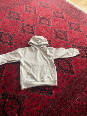 Vit hoodie med magficka - Säljer en enkel och stilren vit hoodie med huva och stor magficka framtill. Hoodien har ribbade muddar vid ärmslut och nederkant. Perfekt för dig som gillar en clean och avslappnad look.
