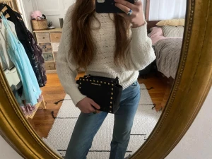 Svart Michael Kors handväska med nitar - Snygg svart handväska från Michael Kors med guldfärgade nitar längs kanterna och logga framtill. Väskan har en boxig form och är tillverkad i slätt läder. Perfekt för dig som vill ha en edgy och trendig accessoar till din outfit.