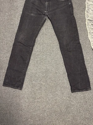 Svarta jeans från Emporio Armani - Säljer ett par svarta jeans från Emporio Armani med klassisk rak passform. Jeansen har fem fickor och är tillverkade i ett mjukt denimtyg som sitter snyggt. Perfekta för dig som gillar stilrena och tidlösa plagg. Ett litet hål som jag har sytt, syns knappt när byxorna är på
