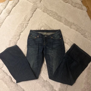 Mörkblå bootcut jeans - Snygga mörkblå bootcut jeans med klassisk femficksdesign och kontrastsömmar. Jeansen har en låg midja och subtila slitningar framtill för en avslappnad look. Perfekta till sneakers eller boots för en trendig vardagsstil.
