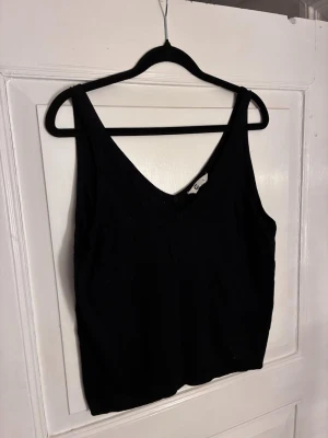 Svart stickad linnetopp med v-ringning Cubus - En svart linnetopp från Cubus med v-ringning och breda axelband. Toppen är stickad och har en enkel, stilren design som är lätt att matcha med olika outfits. Perfekt för dig som gillar en clean och klassisk look. Passar L