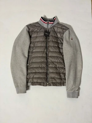 Moncler Cardigan - Grå cardigan jacka från Moncler. Lappen i nacken har lossnat på ena sidan samt lite missfärgning på ryggen som endast syns vid nära inspektion annars riktigt fint skick. Storlek XL sitter som en medium/large.