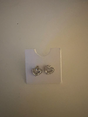 Silvriga hjärtformade örhängen - Säljer ett par söta silvriga örhängen i form av hjärtan, dekorerade med små glittrande stenar runt hela kanten , helt oandvända 💕