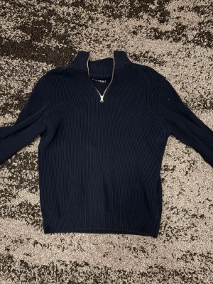 Mörkblå ribbad ziptröja - Mörkblå ribbad tröja med halv dragkedja och hög krage. Tröjan har lång ärm och är tillverkad i ett mjukt, stretchigt material. Perfekt för en stilren och avslappnad look.