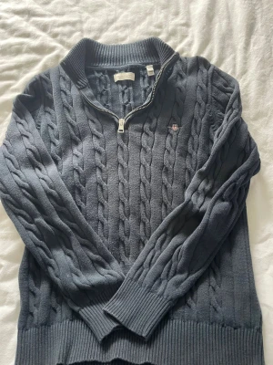 Mörkgrå kabelstickad tröja Gant - Snygg mörkblå kabelstickad tröja från Gant med halv dragkedja och ribbade muddar. Tröjan är i storlek 146/152cm. Köpte den för cirka 900kr och använt den endast 2-3 gånger.