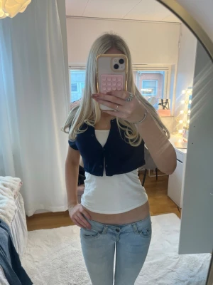 Mörkblå croppad bolerotopp - Snygg mörkblå croppad bolerotopp med korta ärmar och knappar framtill. Perfekt att styla över ett linne eller topp för en trendig lager-på-lager-look. Enkel och stilren design som passar till mycket.