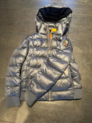 Mörkblå dunjacka från Parajumpers - Snygg mörkblå dunjacka från Parajumpers med huva och ribbade muddar. Jackan har en patch på ärmen, men syns nästan inte, två sidofickor med dragkedja och quiltad design. Perfekt för kalla dagar och riktigt trendig look. Är som en liten Small ungefär. 