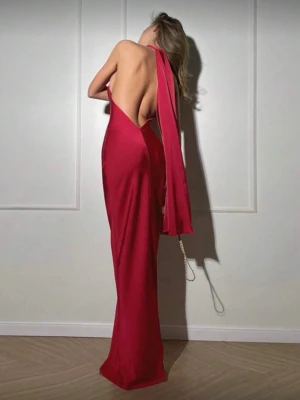 Röd långklänning med öppen rygg - Snygg röd långklänning i satinliknande material med hög hals och öppen rygg. Klänningen har en elegant, figurnära passform och ett långt band som faller ner från halsen. Perfekt för dig som vill sticka ut med en stilren look.