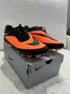 Nike Hypervenom orange fotbollsskor - Säljer ett par Nike Hypervenom fotbollsskor i orange och svart med snygg design och låg profil. Skorna har fasta dobbar och är tillverkade i syntetmaterial för bra grepp och kontroll på planen. Perfekta för dig som vill sticka ut på matchen!