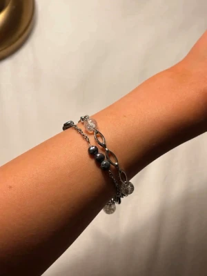 Armband med pärlor - Snyggt armband i silverfärg med både lila och genomskinliga pärlor. Armbandet har en tunn kedja och dekorativa länkar som ger en trendig look. Perfekt accessoar för dig som gillar stilrena detaljer och vill addera lite extra till din outfit.