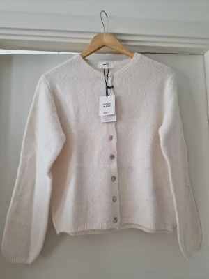 Krämvit kofta i alpackablandning - Mysig krämviit kofta från Gina Tricot i mjuk alpackablandning. Klassisk rak modell med rund halsringning och silverfärgade knappar framtill. Perfekt att slänga över en t-shirt eller topp för en clean look. Storlek XS