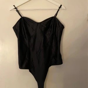Svart satin korsett-topp med smala band - Snygg svart korsett-topp body i satin med smala axelband och markerade kupor. Toppen har en glansig finish och en figurnära passform med spetsig nederkant. Perfekt för att skapa en trendig look EJ MINA BILDER!!💕