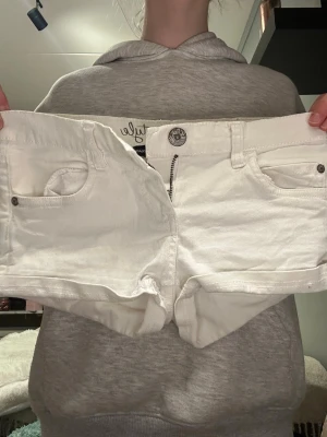 Vita lågmidjade shorts från Only - Säljer ett par vita jeansshorts från Only med klassisk femficksdesign, knappgylf och bälteshällor. Shortsen är i stretchigt denimtyg och har en låg midja. Perfekta för sommaren och enkla att matcha med olika stilar. Måste rensa ut shorts och det är därför jag säljer dem här shortsen💞