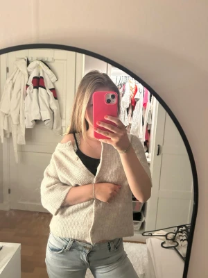 Beige ribbad stickad blus med knappar - Supermysig beige stickad blus med ribbat material och knappar framtill. Modellen är croppad med v-ringning och trekvartsärm, perfekt för lager-på-lager och chill vibes. Snygg att bära off-shoulder för en avslappnad look.