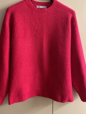 Knallrosa stickad tröja från Zara - En snygg, gosig och varm stickad tröja från Zara i en stark rosa färg. Tröjan har rund halsringning, raka axlar och långa ärmar. Ribbstickade muddar vid ärmslut och nederkant ger en clean look. Perfekt för dig som vill sticka ut lite extra. Passar storlek M också.