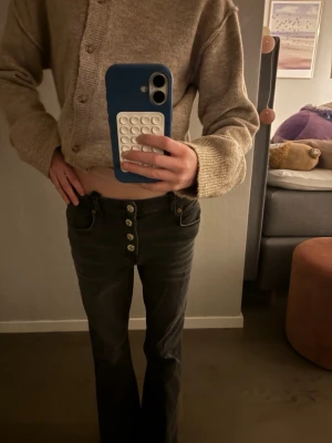 Svarta bootcut jeans med knappar - Säljer ett par svarta bootcut jeans och fyra synliga silverknappar framtill. Jeansen har klassiska fickor fram och bak samt lätt utsvängda ben. Perfekta för en trendig look 🪅