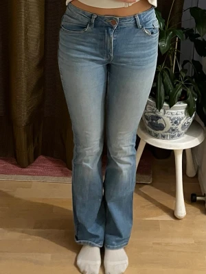 Ljusblå bootcut jeans - Säljer ett par ljusblå bootcut jeans med klassisk femficksdesign och normal midja. Jeansen har en snygg tvätt och är tillverkade i ett mjukt denimtyg med lite stretch för extra komfort. Perfekta för en avslappnad och trendig look.