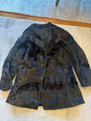 Svart pälskappa i kortare modell, storlek M - Elegant svart pälsjacka i äkta päls med en rak klassisk design. Jackan har en bred krage och knäppning framtill. Insidan är fodrad med ett mörkt tyg med diskreta mönster. Lagad i armhålorna, men överlag väldigt bra skick. Jag vet dessvärre inte vilken typ av päls det är och kappans nypris, men jag har köpt den för 5300kr. Jag bedömer storleken som M, och har storlek 38-40 i storlek annars.  Ärmarna är 55 cm långa från axelsömmmen och kappan är 77 cm lång. 