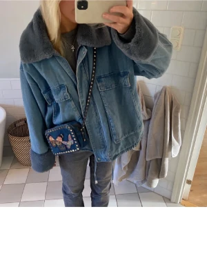 Oversized jeansjacka med fuskpäls - Säljer en oversized blå jeansjacka med bred krage och muddar i grå fuskpäls. Jackan har stora fickor framtill och en avslappnad passform som ger en cool och trendig look. Perfekt för dig som vill ha en unik jeansjacka med extra detaljer. Hör gärna av er vid frågor💕