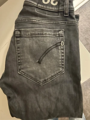 Grå jeans från dondup  - Säljer ett par gråa slim fit jeans från dondup med snyggt slitna detaljer och klassisk femficksmodell. Jeansen har en diskret D-logga vid bakfickan och kontrastsömmar som ger en cool look. Perfekta för dig som gillar streetwear och vill ha en avslappnad stil.