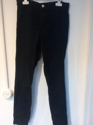 Svarta skinny jeans &Denim - Säljer ett par svarta skinny jeans från &Denim med hög midja och ankellängd. Jeansen har klassisk femficksdesign och stängs med knapp och dragkedja. Perfekta för dig som gillar en tight passform och stilren look.