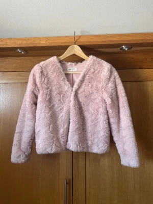 Ljusrosa fuskpälsjacka H&M - Mysig ljusrosa fuskpälsjacka från H&M med mjukt foder och dold knappstängning framtill. Jackan har en rak passform och långa ärmar, perfekt för att hålla värmen under kalla dagar. Trendig och fluffig look som lyfter vilken outfit som helst.perfekt för våren
