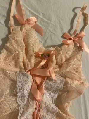 Ny! Spetsbody med rosetter och blommor - Ny! Jättesöt romantisk spetsbody med rosetter och blommor. Köptes för 5 år sedan men aldrig använd pga inte min storlek. Storlek S men passar som XS/S och har justerbara axelband. 