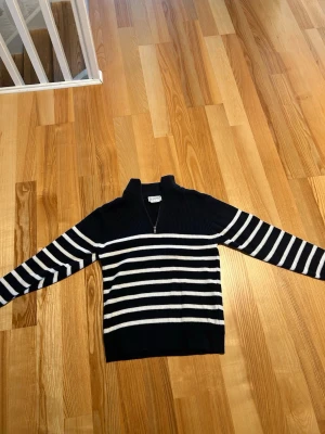 Marinblå stickad tröja med dragkedja - Säljer en marinblå stickad tröja från COPE med vita horisontella ränder och halv dragkedja vid halsen. Tröjan har lång ärm och ribbade muddar. Perfekt för en stilren och avslappnad look.