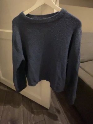 Blå stickad tröja från 157 - Mysig blå stickad tröja från 157 i storlek XS. Tröjan har en enkel, rak passform med rund halsringning och långa ärmar. Perfekt för kyliga dagar och lätt att matcha med olika outfits. finns en liten reva på ena armen. 