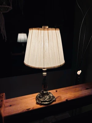 Klassisk bordslampa med tygskärm - Säljer en elegant bordslampa med veckad beige tygskärm och dekorativa gulddetaljer. Lampfoten är i metall med antik finish och har fina ornament. Perfekt som mysbelysning i sovrum eller vardagsrum.