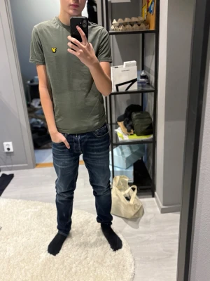 Olivgrön t-shirt från Lyle & Scott - Snygg olivgrön t-shirt från Lyle & Scott med klassisk gul logga på bröstet. T-shirten har rund hals, korta ärmar och är gjord i mjuk bomull. Perfekt basplagg som funkar till det mesta.