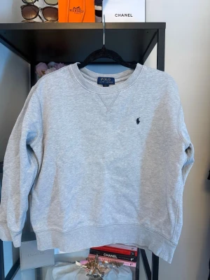 Grå sweatshirt från Polo Ralph Lauren - Klassisk grå sweatshirt från Polo Ralph Lauren med rund halsringning och den ikoniska lilla marinblå logon broderad på bröstet. 