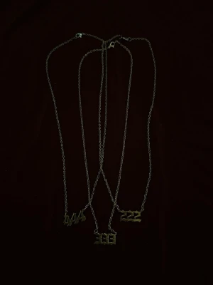 Guldiga nummerhalsband - Säljer tunna halsband i metall med hängen i form av siffrorna 222, 333, 444 i gotisk stil. Kedjorna är guldfärgade. Perfekt accessoar för dig som gillar unika detaljer och vill sticka ut med personliga smycken.