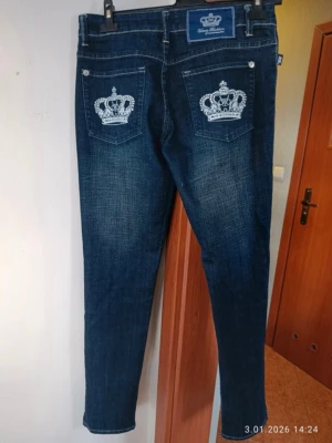 Mörkblå lågmidjade jeans i storlek W30 L32 från Victoria Beckham  - Säljer ett par mörkblå jeans från Victoria Beckham i storlek W30 L32 med smala raka ben och snygg slitning. Bakfickorna har vita broderade kronor som ger en unik touch. Klassisk femficksmodell med silverfärgade knappar och detaljer. Perfekta för dig som gillar statement-plagg.
